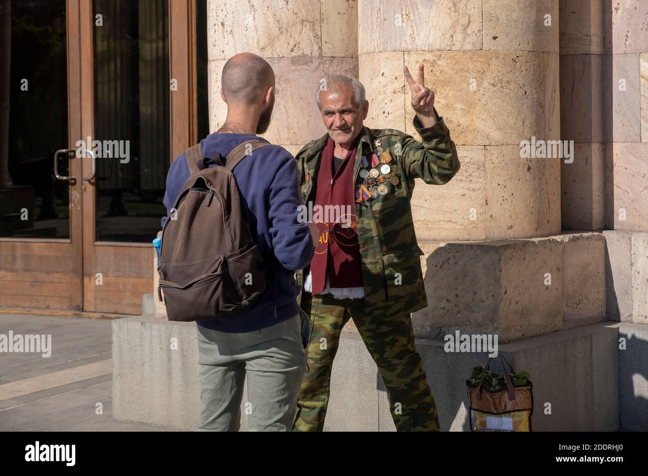 A reporter of Radio France Internationale, usually referred to as RFI  speaks to an elderly Armenian man which wears honor medals and marks the  victory sign during a military conflict between Armenian