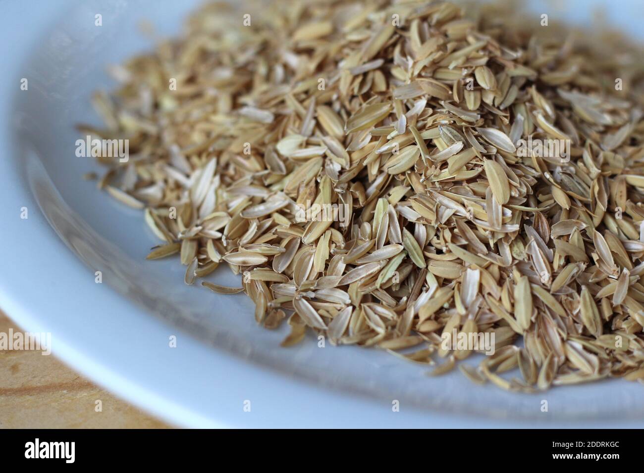 A pile of rice hulls (husks) in close up on a white plate on a wooden table. Husks are a waste product which can be reused in compost making and as a Stock Photo