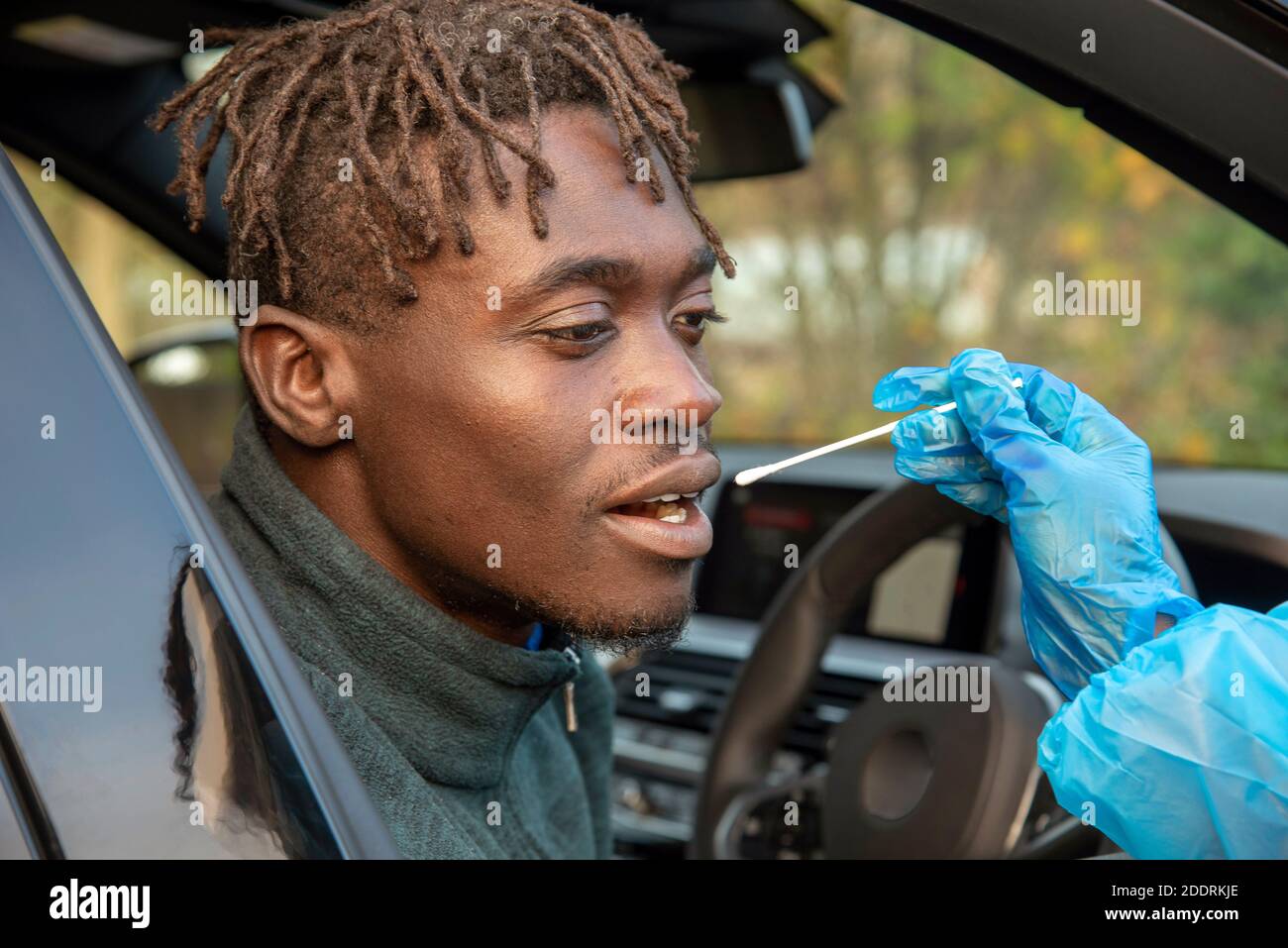 Southern England, UK. 2020.  Black client at Covid-19 testing centre having  siliva sample taken with a cotton bud by a female tester. Stock Photo