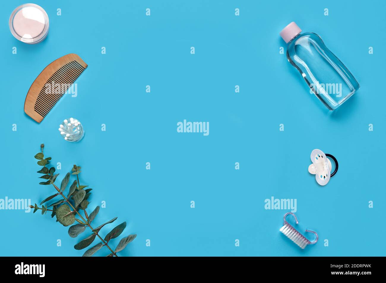 Wooden hair comb, cotton pads, pacifier, bottle with transparent liquid, cotton swabs, brush and green twig on blue background. Close up, copy space Stock Photo