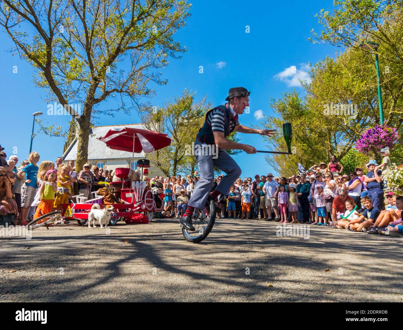 Traditional clown performing on a unicycle outside to a village crowd in Plovan in Brittany north west France during the 15 August public holiday. Stock Photo