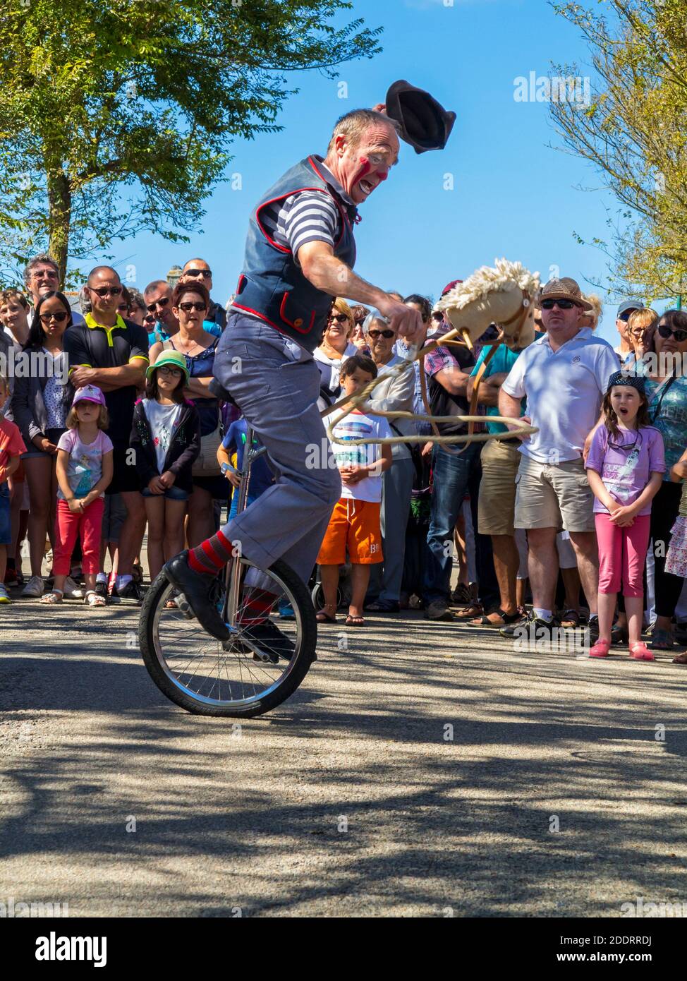 Traditional clown performing on a unicycle outside to a village crowd in Plovan in Brittany north west France during the 15 August public holiday. Stock Photo
