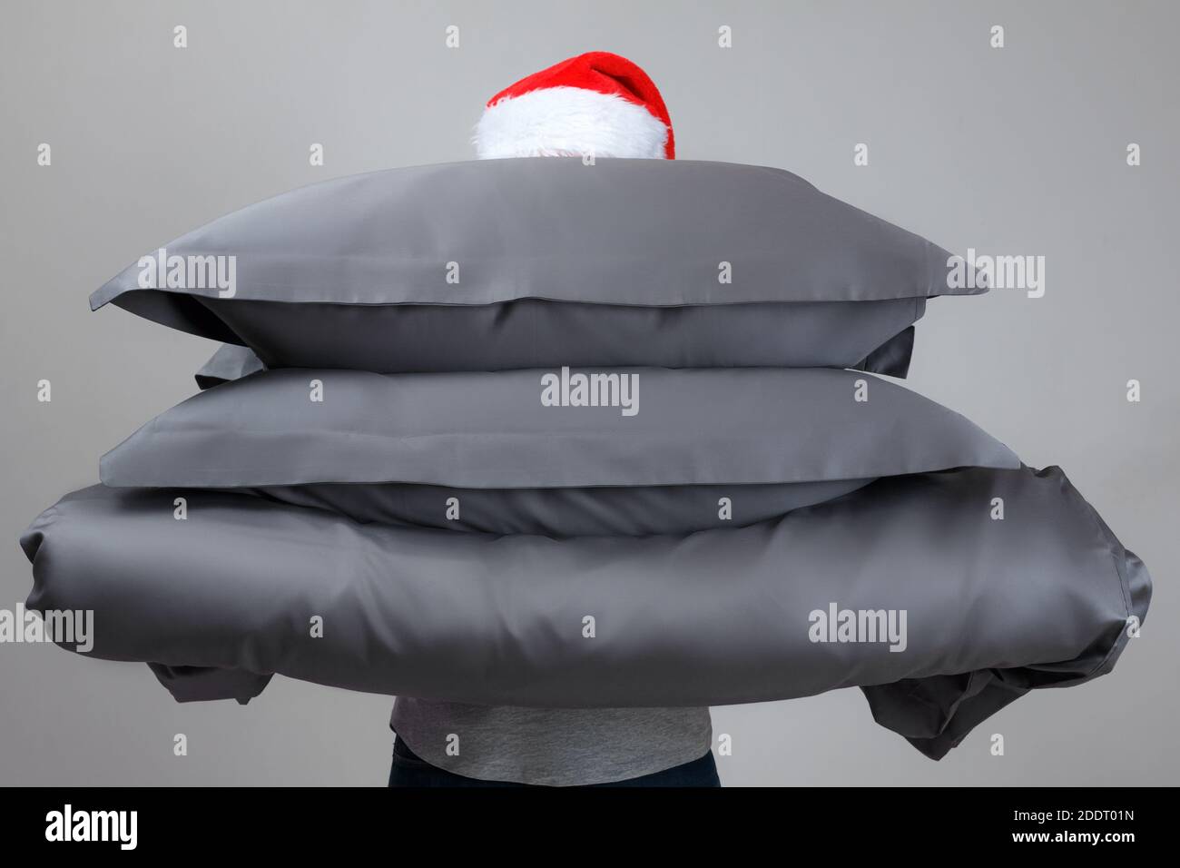 Woman in Santa Claus hat holding a warm duvet and feather pillows of gray. Bedding for sleeping. Stock Photo