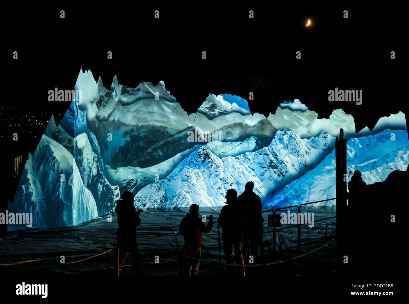 Silhouettes of people watching Winter mountain landscape projection with crescent moon, Edinburgh Zoo, Scotland, UK Stock Photo