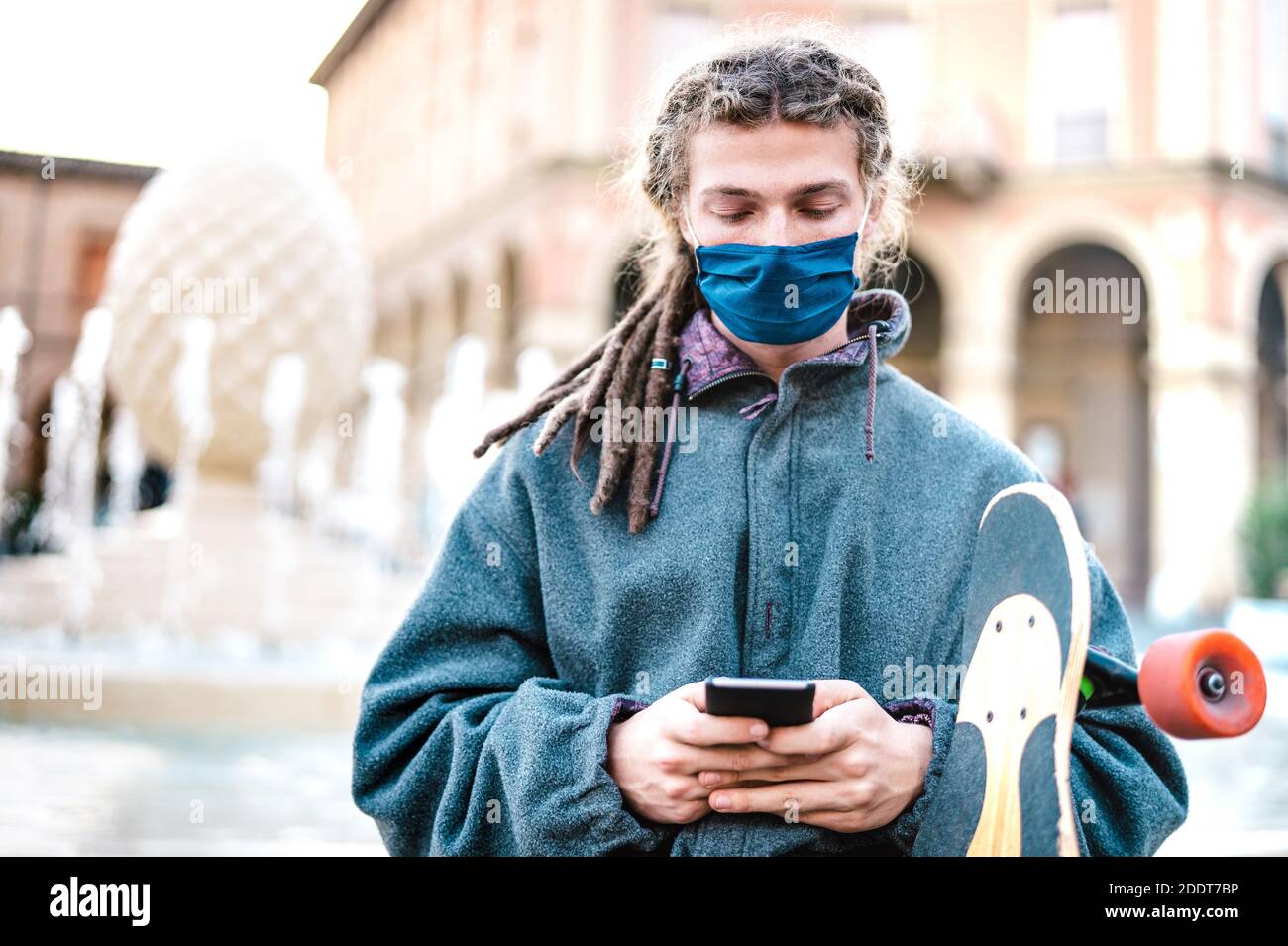 Unhappy guy with protective mask using tracking app on mobile smartphone - Young worried millenial sharing content on social media Stock Photo