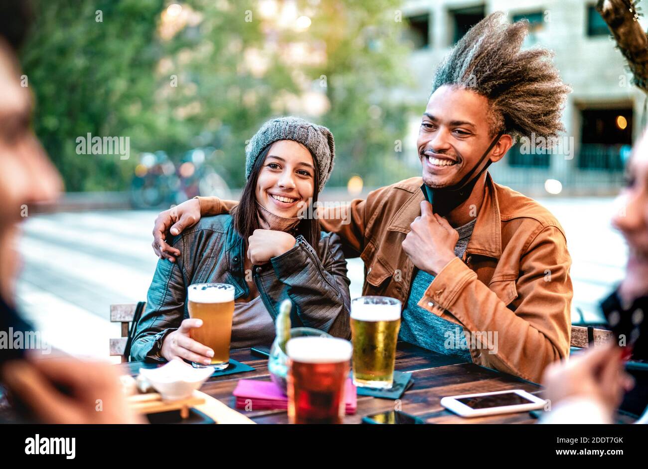 Young couple drinking beer glasses with open face masks - New normal lifestyle concept with friends having fun together on happy hour at brewery bar Stock Photo