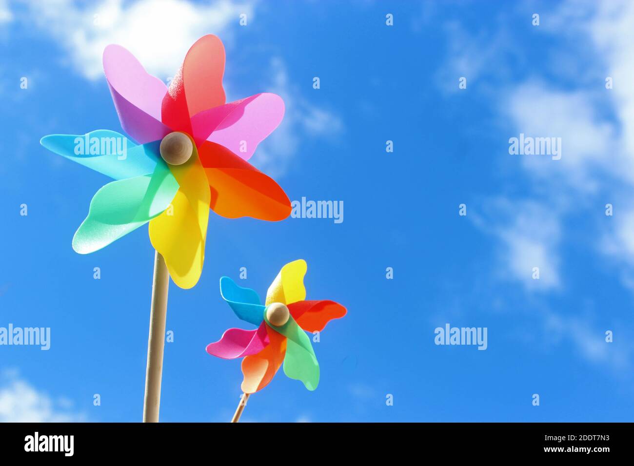a small and a large pinwheel toy, blue sky with white clouds Stock Photo