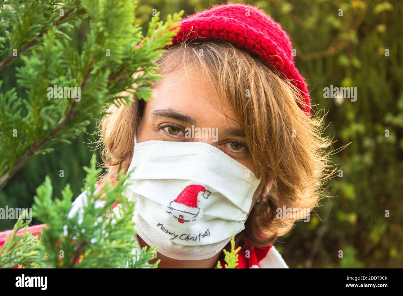 Young man celebrating Christmas with protective medical face mask due to covid-19 pandemic. Young man draws santa hat on a face mask and celebrating C Stock Photo