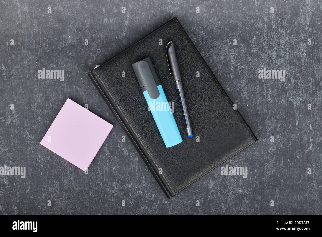 Ball pen and a marker lie on a black diary, next to paper sticks for pink records, business still life Stock Photo