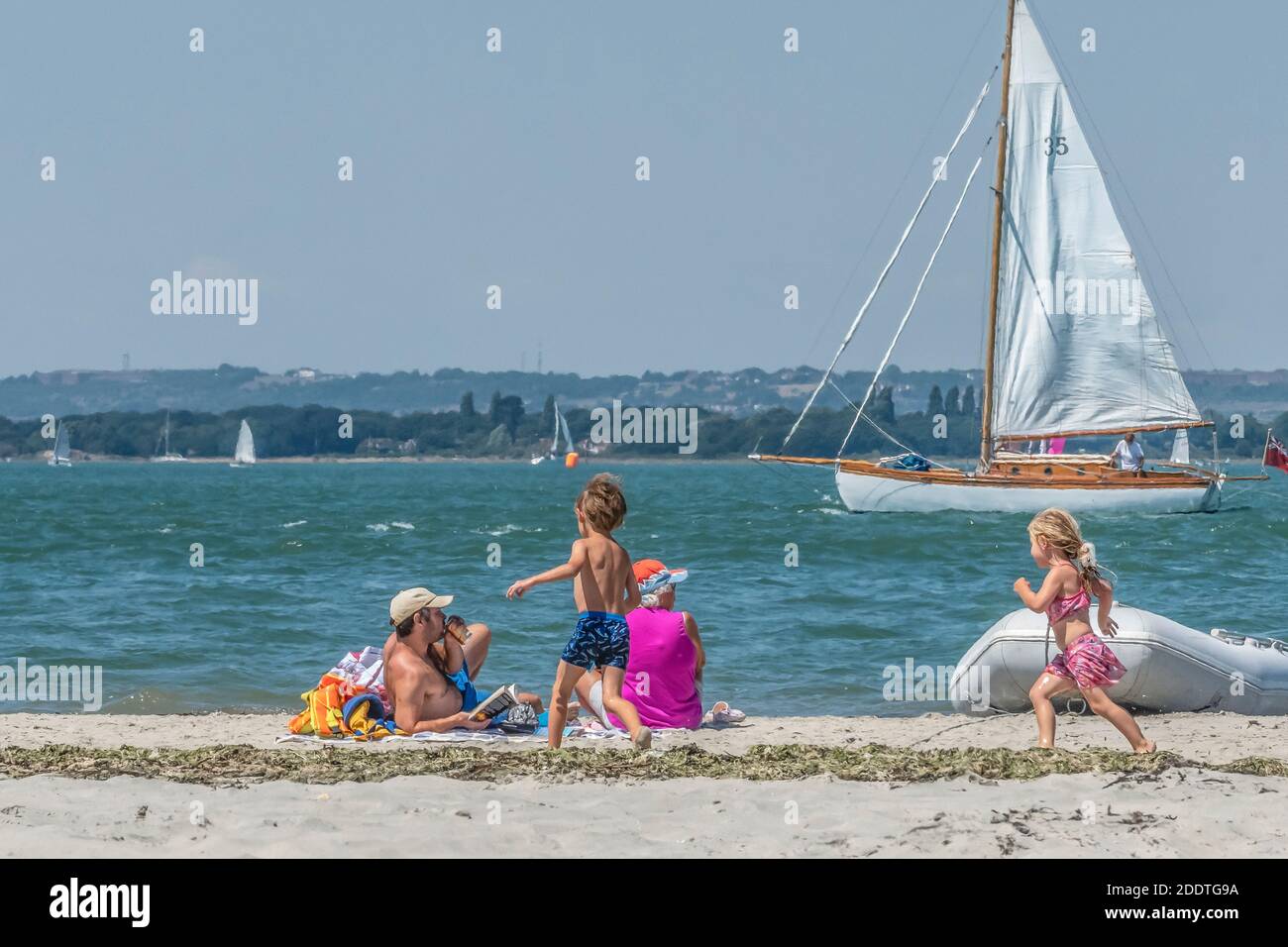 Family With Children Play On The Sandy Beach At West Wittering With Yacht Sailing In Chichester Harbour West Sussex England Uk Stock Photo Alamy