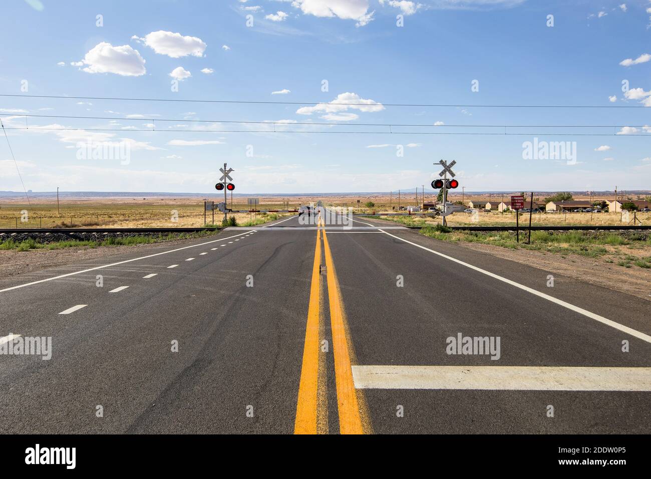 A track railway  crossing on the two-lane rural Mojave desert highway - old Route 66. Dry arid envirnoment under a cloudy blue sky - A red-light railw Stock Photo