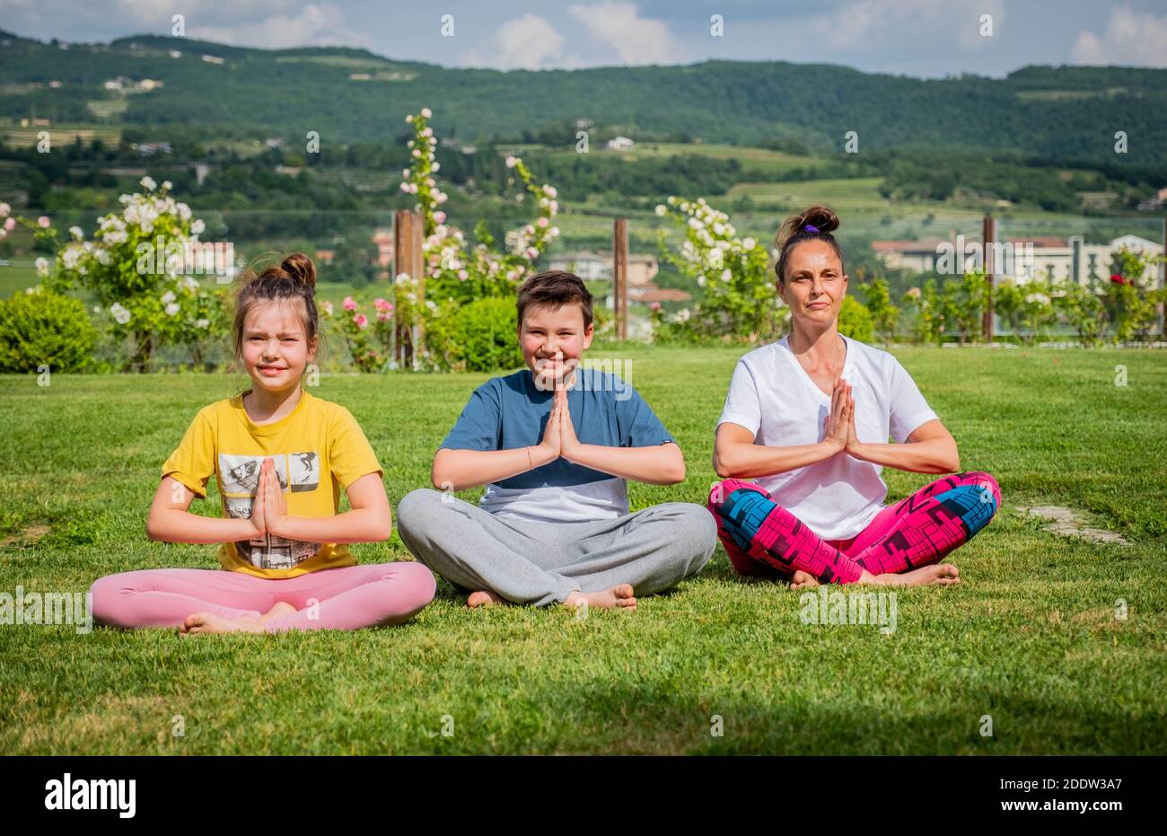 Mother and her children doing yoga exercises outdoors - Young woman doing fitness exercises in the park - Achieving harmony Stock Photo