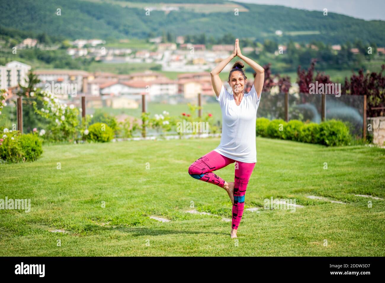 Beautiful woman doing yoga in the garden with beautiful landscape - Young mother is doing a yoga pose for balance and stretching - Fitness mum Stock Photo