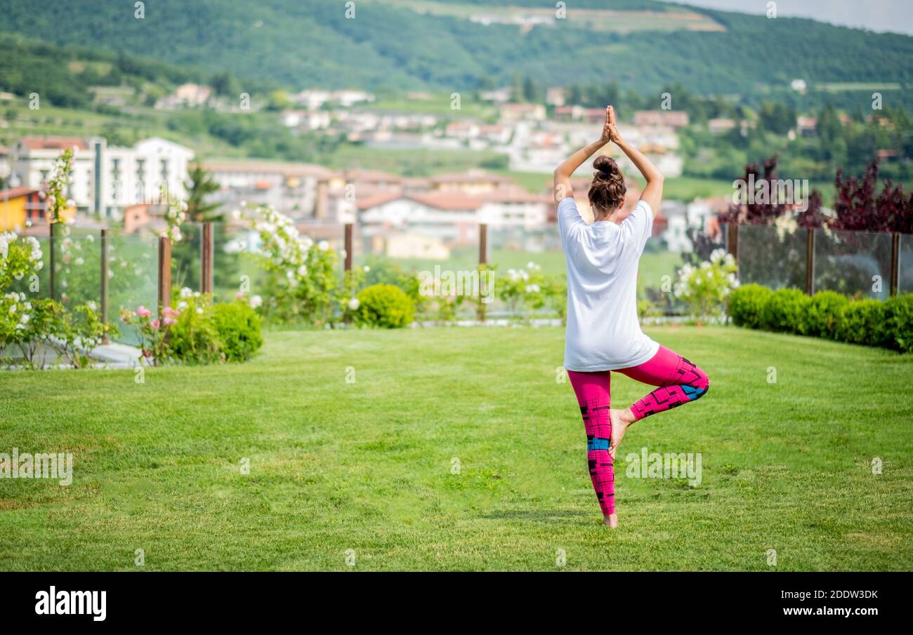 Beautiful woman doing yoga in the garden with beautiful landscape - Young mother is doing a yoga pose for balance and stretching - Fitness mum - Athle Stock Photo