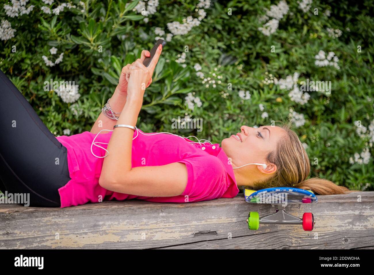 Portrait of beautiful girl lying on the skateboard and listening to music with her smartphone - Girl lying on the skateboard looks at the phone, smile Stock Photo
