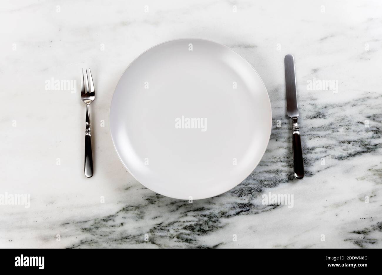 Dinner setting with clean plate, knife and fork on marble table Stock Photo