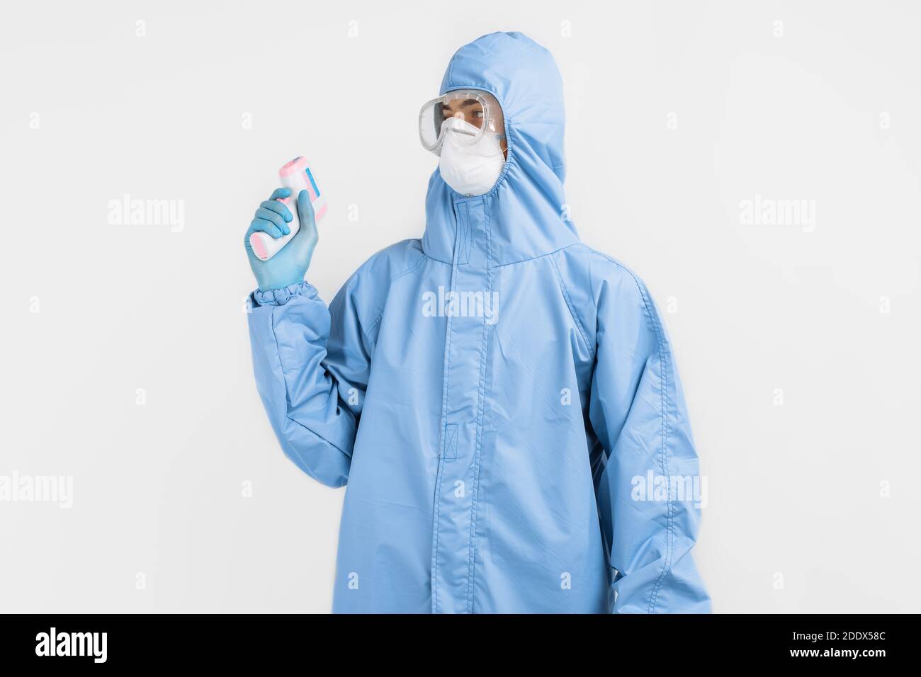doctor in a protective suit from the coronavirus, a medical mask glasses and gloves, uses an infrared non-contact thermometer gun to check body temper Stock Photo