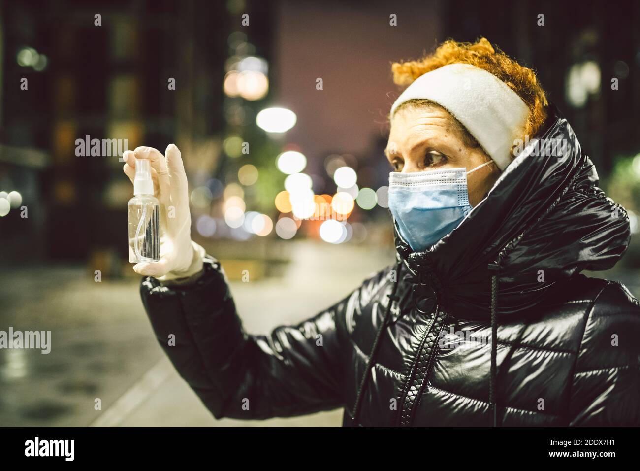 Mature woman with face mask and rubber medical gloves holds antiseptic ...