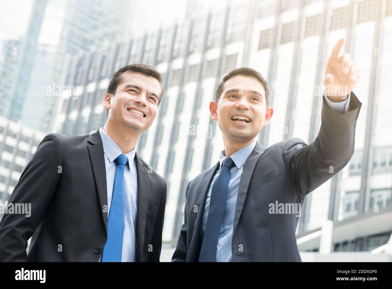 Two businessmen standing outdoors in the city with one hand pointing out - business partner and co-worker concepts Stock Photo