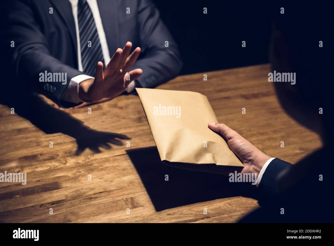 Businessman rejecting money in the envelope secretly offered by his partner in the dark - anti bribery concept Stock Photo