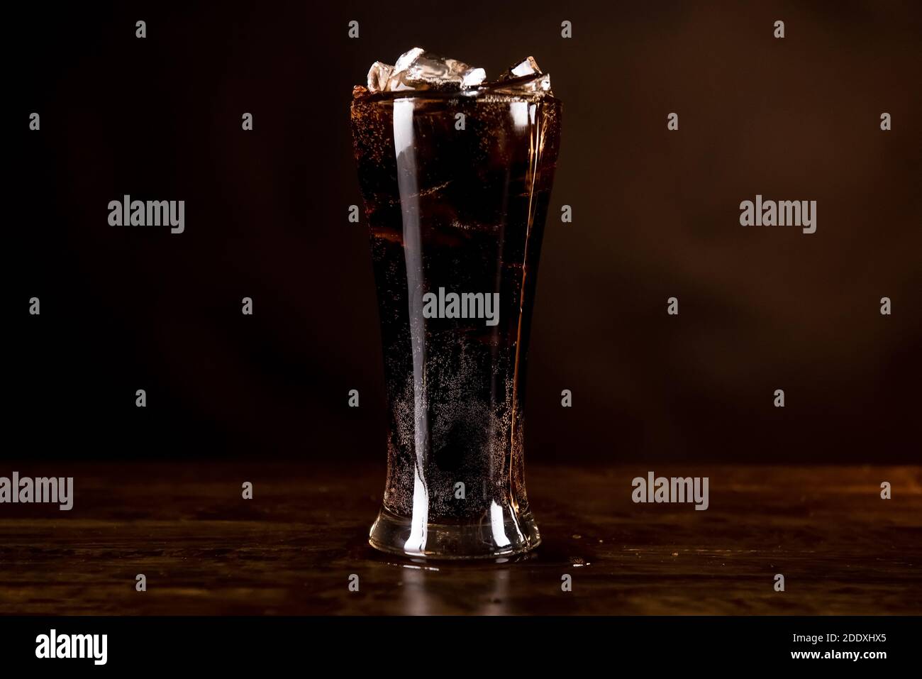 Glass of cold refreshing carbonated cola soft drink with full of ice cubes on wood counter bar in dark background Stock Photo