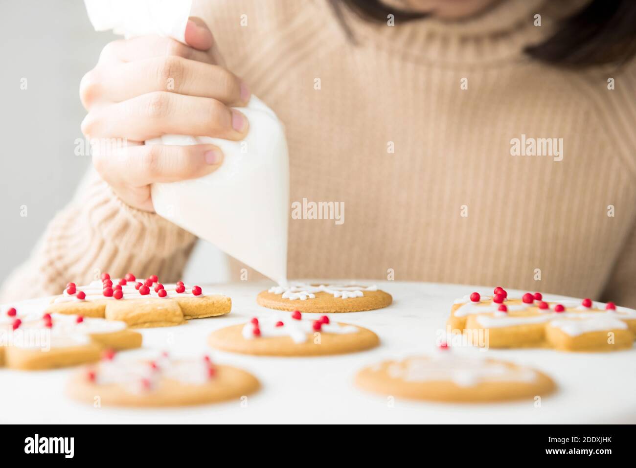 Young woman decorating homemade gingerbread Christmas cookies with royal icing sugar on white platter at bakery Stock Photo