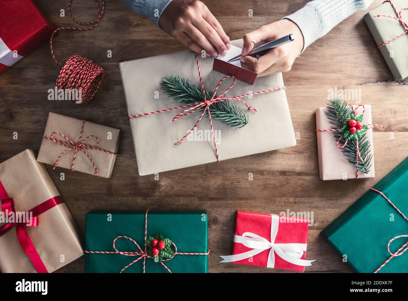 Woman writing Christmas greeting card on gift box at the table, top view Stock Photo