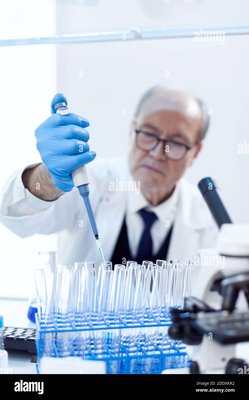 Senior pharmaceutical scientist in modern laboratory using dropper dispenser with genetic material. Professional chemist using pippete with blue solution for microbiology tests. Stock Photo