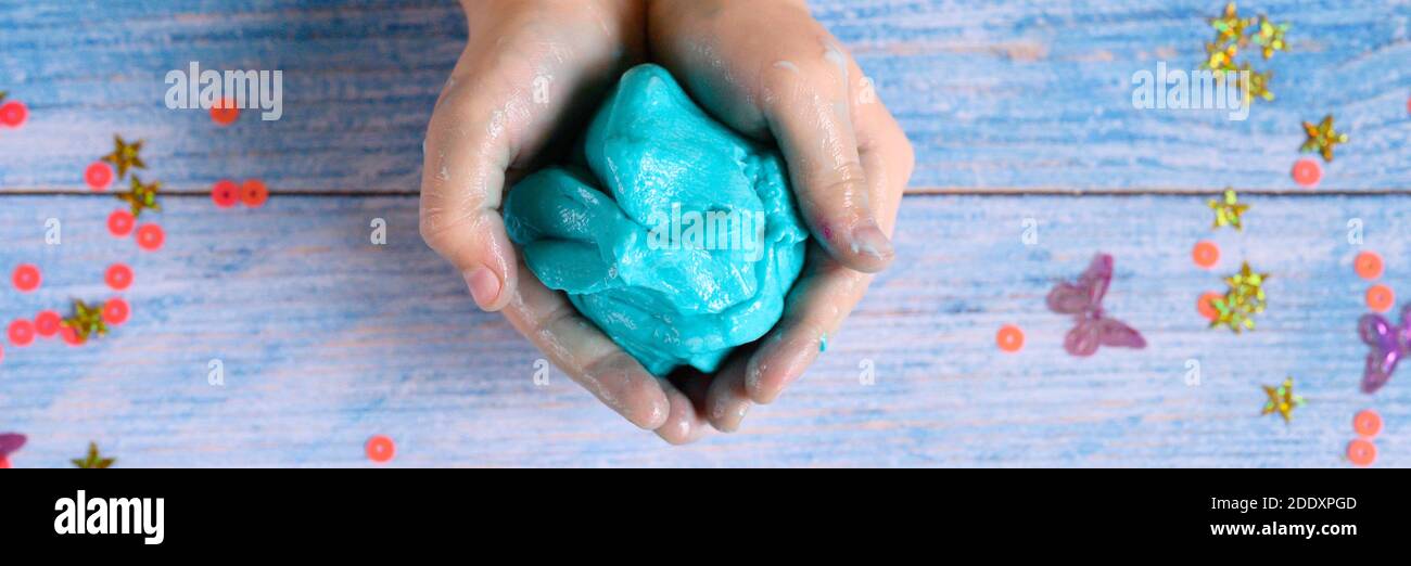 a little girl hands making slime herself on blue wooden background. banner Stock Photo