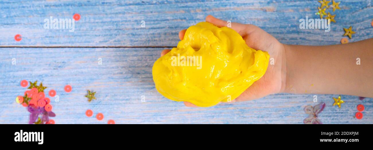 a little boy hand playing yellow slime on blue wooden background. banner Stock Photo