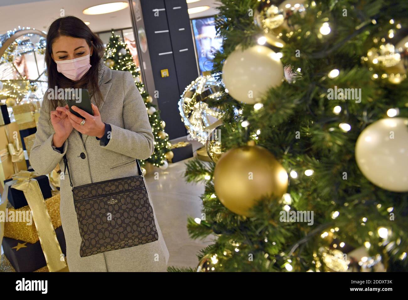 Topic picture prisoners in the coronavirus pandemic on November 26th, 2020. A young woman with face mask and mask is standing with her smartphone, cell phone behind a Weihaftertsbaum and looks at it. Mall, shopping center, pandemic, lockdown, shutdown, incidence value. MODEL RELEASED! | usage worldwide Stock Photo