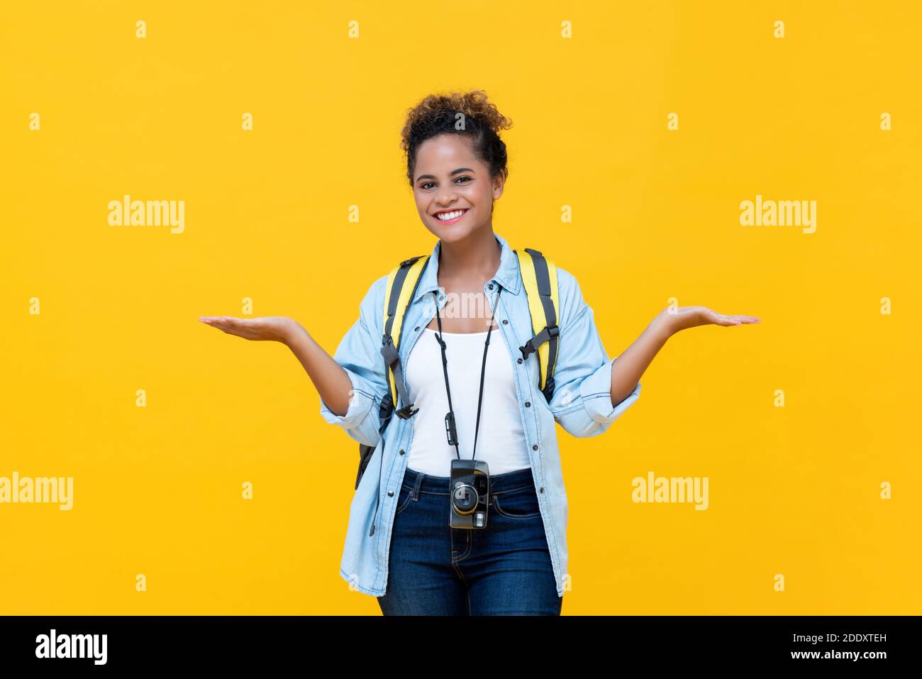 Beautiful young African American woman tourist backpacker doing no worry gesture with open hands isolated on yellow studio background Stock Photo