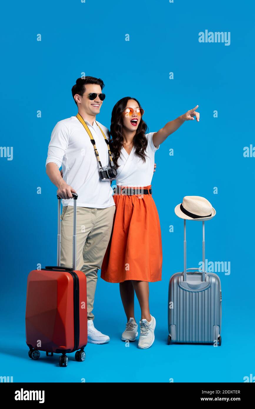 Happy smiling interracial tourist couple with baggage enjoying their summer vacation getaway together in blue studio background Stock Photo