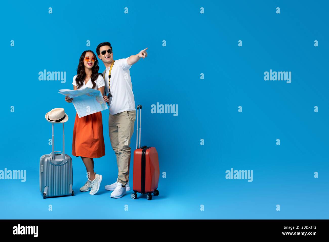 Happy smiling interracial tourist couple with baggage enjoying their summer vacation getaway together in blue studio background Stock Photo