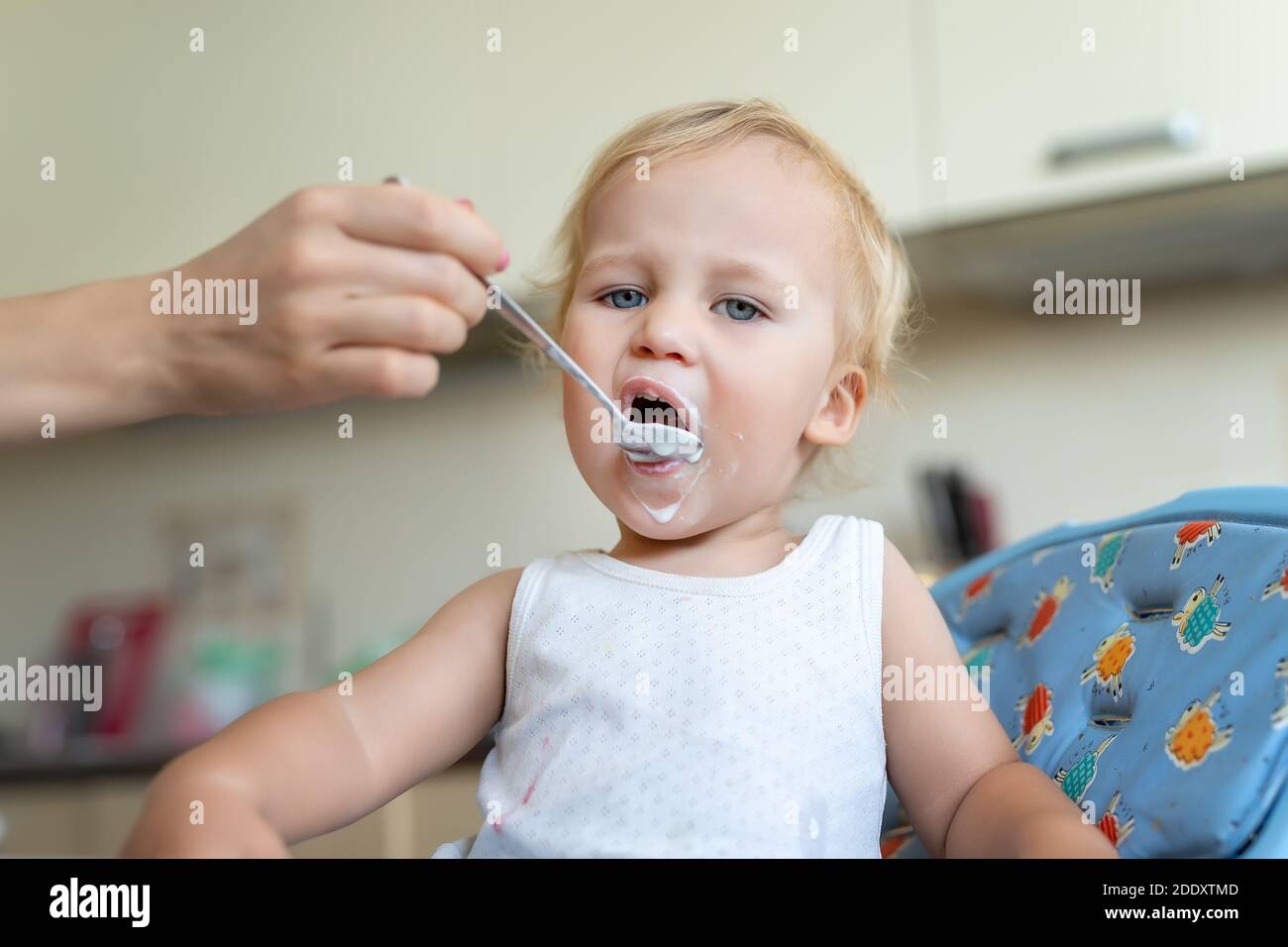 Mother feeding cute adorable caucasian little blond toddler boy with