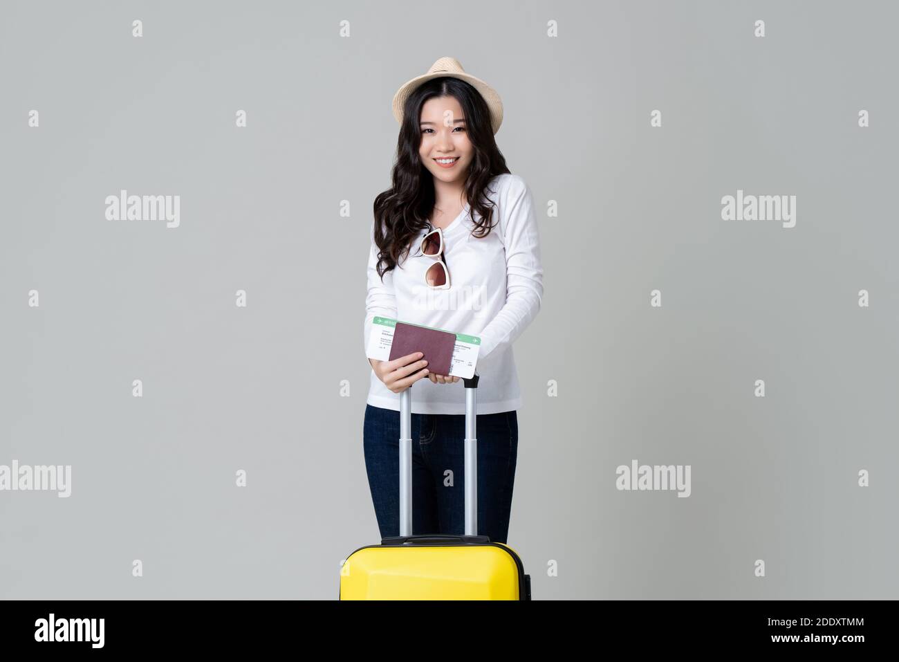 Happy young Asian woman tourist with baggage passport and boarding pass ready for travelling isolated on gray studio background Stock Photo