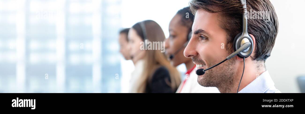 Smiling friendly Hispanic man working with team as telemarketing customer service agents in call center office banner background Stock Photo