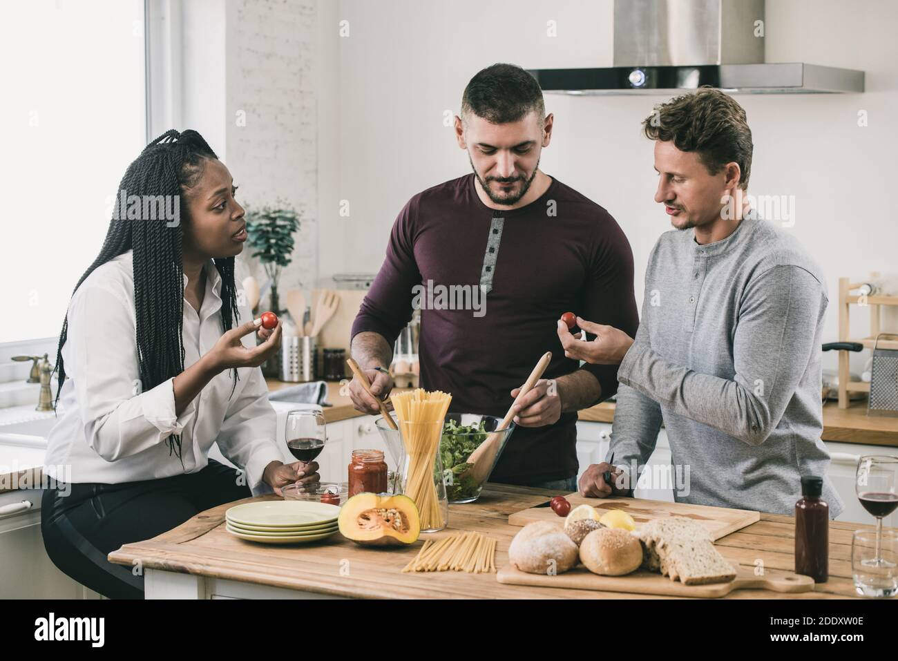 African American woman with two Caucasian men cooking salad together in kitchen at home on weekend Stock Photo