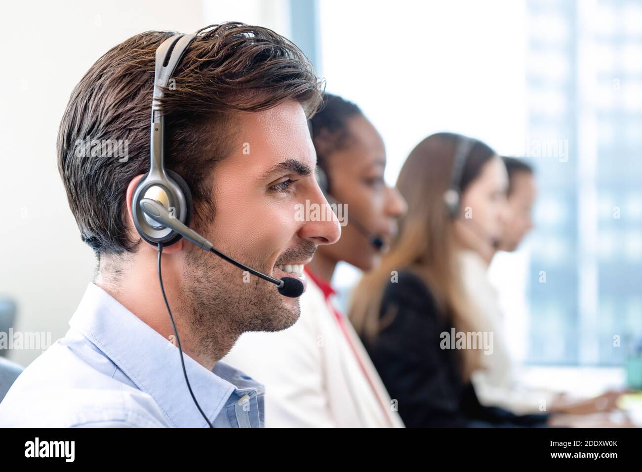 Smiling friendly Hispanic man working in call center office with team as telemarketing customer service agents Stock Photo