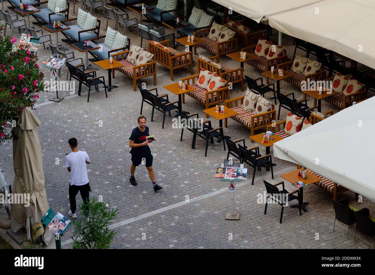 Tourists pass empty restaurants - due to an 87% decline in tourism in 2020 - in the usually busy Thissio area of Central Athens Greece Stock Photo