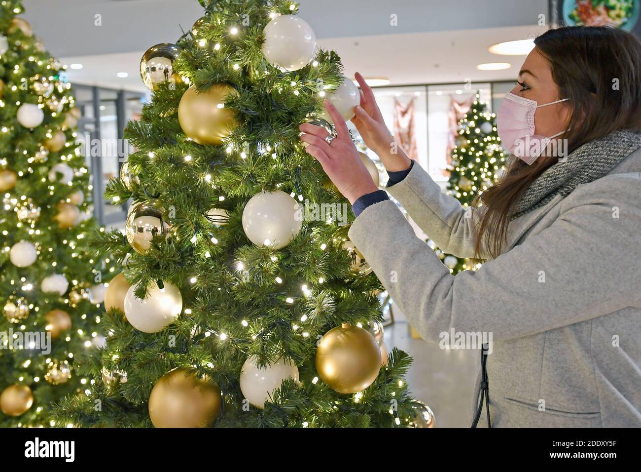 Topic picture prisoners in the coronavirus pandemic on November 26th, 2020. A young woman with face mask, mask stands in front of a Weihaftertsbaum and decorates it, pandemic, lockdown, shutdown, incidence value. MODEL RELEASED! | usage worldwide Stock Photo