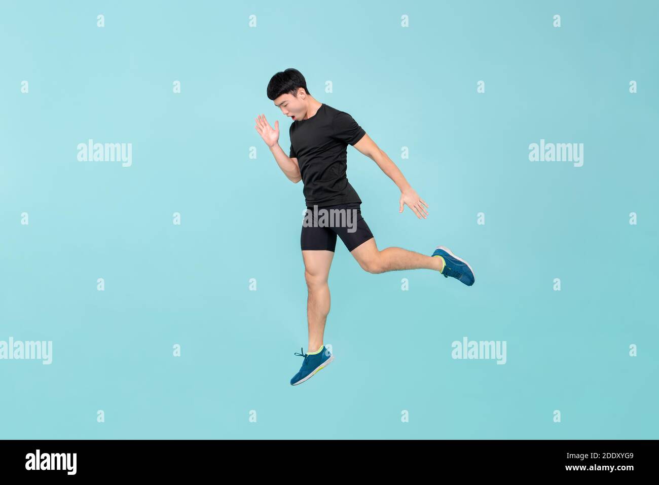 Full body of energetic young athlete Asian man jumping in light blue studio background Stock Photo