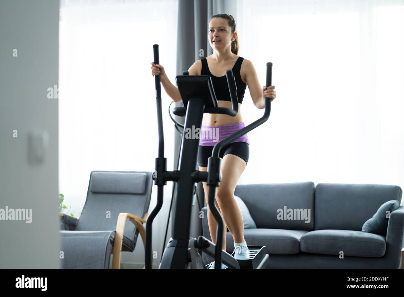 Woman Training On Elliptical Trainer At Home Stock Photo