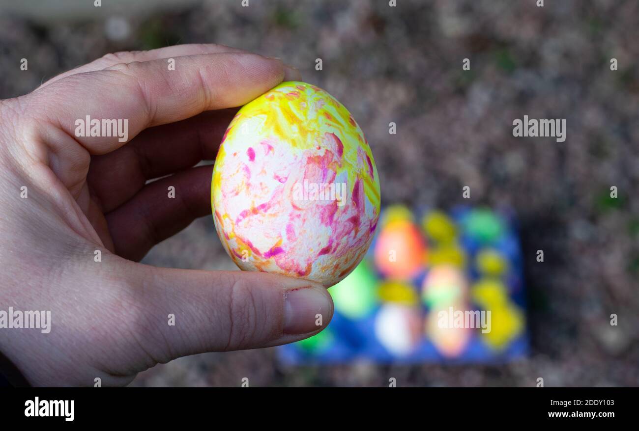 Hand holding up a boiled egg that has been handpainted in different colors - a tradition for Easter holiday in Sweden. Stock Photo