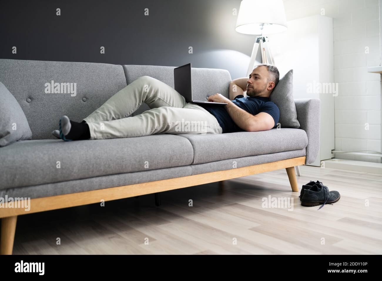 Man Lying In Sofa At Home And Using Laptop Stock Photo