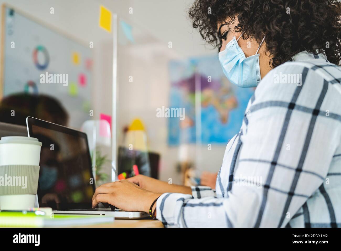 Young people in co-working creative space wearing surgical mask protection and keeping social distance to avoid corona virus spread Stock Photo