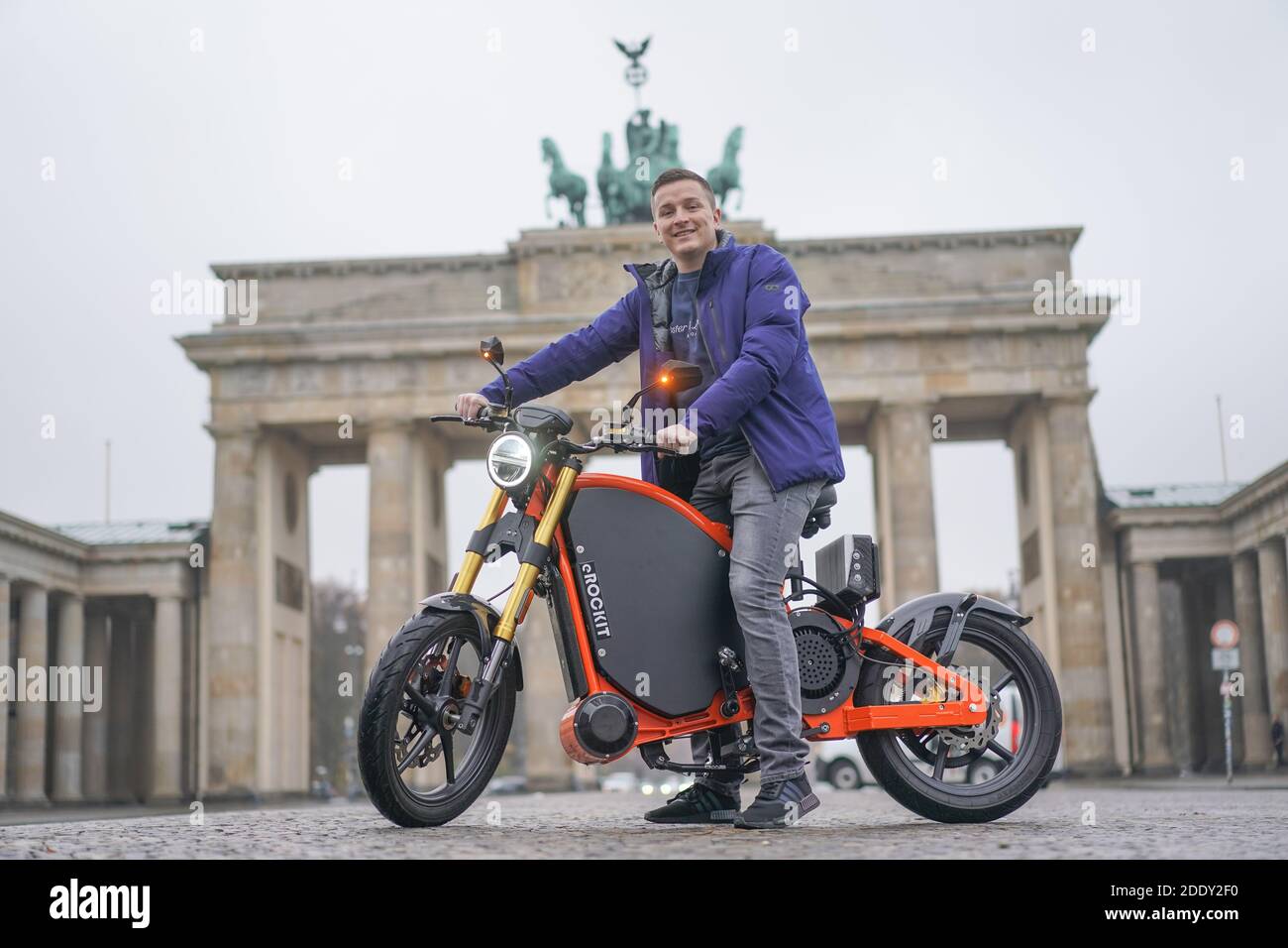 27 November 2020, Berlin: Aaron Trosche, moderator, influencer and start-up entrepreneur, sits on an eROCKIT in front of the Brandenburg Gate. The content marketing professional has invested in the Brandenburg vehicle manufacturer eROCKIT Systems. In the pedal-controlled electric motorcycle, the electronics register the muscle power used by the rider and multiply it many times over. With a slight pedalling movement, you can reach up to 89 km/h. Photo: Jörg Carstensen/dpa Stock Photo