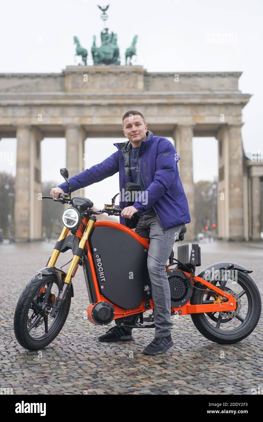 27 November 2020, Berlin: Aaron Troschke, moderator, influencer and start-up entrepreneur, sits on an eROCKIT in front of the Brandenburg Gate. The content marketing professional has invested in the Brandenburg vehicle manufacturer eROCKIT Systems. In the pedal-controlled electric motorcycle, the electronics register the muscle power used by the rider and multiply it many times over. With a slight pedalling movement, you can reach up to 89 km/h. Photo: Jörg Carstensen/dpa Stock Photo