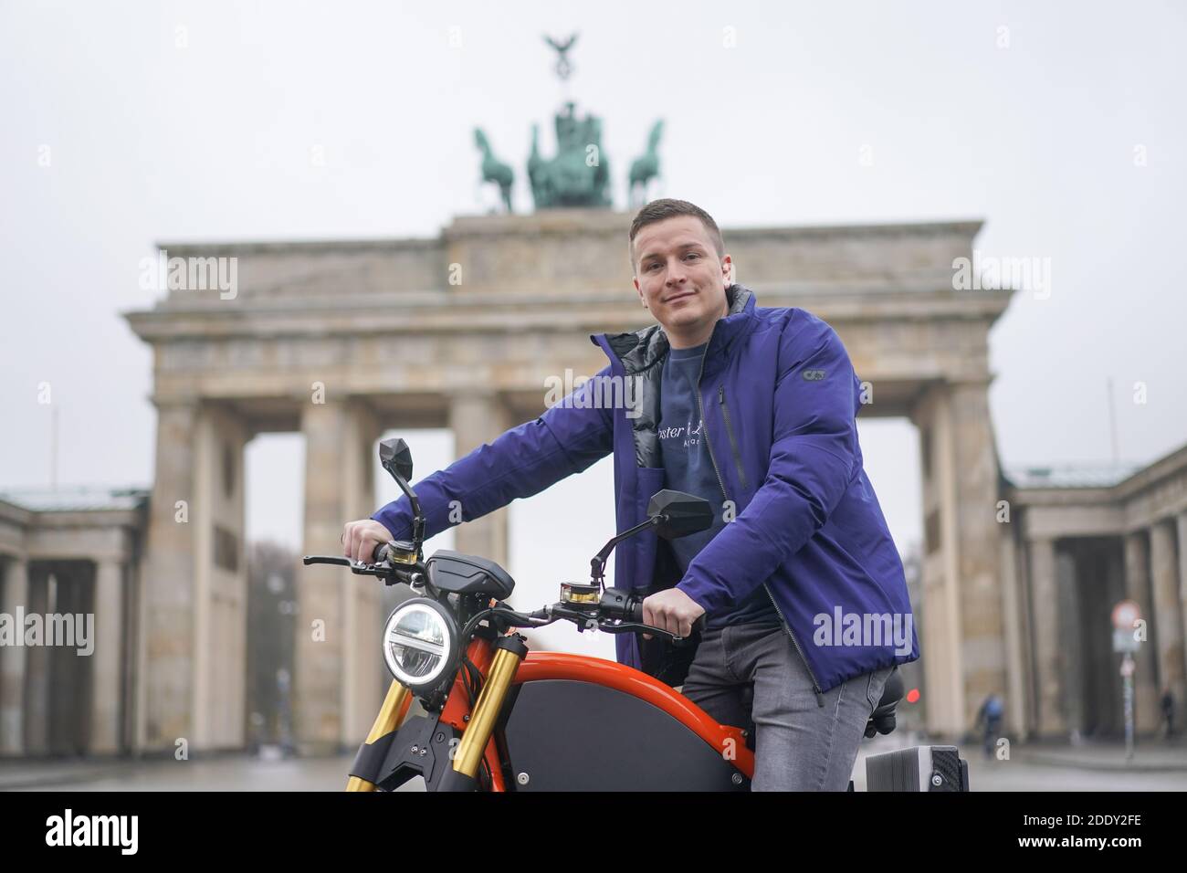 27 November 2020, Berlin: Aaron Troschke, moderator, influencer and start-up entrepreneur, sits on an eROCKIT in front of the Brandenburg Gate. The content marketing professional has invested in the Brandenburg vehicle manufacturer eROCKIT Systems. In the pedal-controlled electric motorcycle, the electronics register the muscle power used by the rider and multiply it many times over. With a slight pedalling movement, you can reach up to 89 km/h. Photo: Jörg Carstensen/dpa Stock Photo