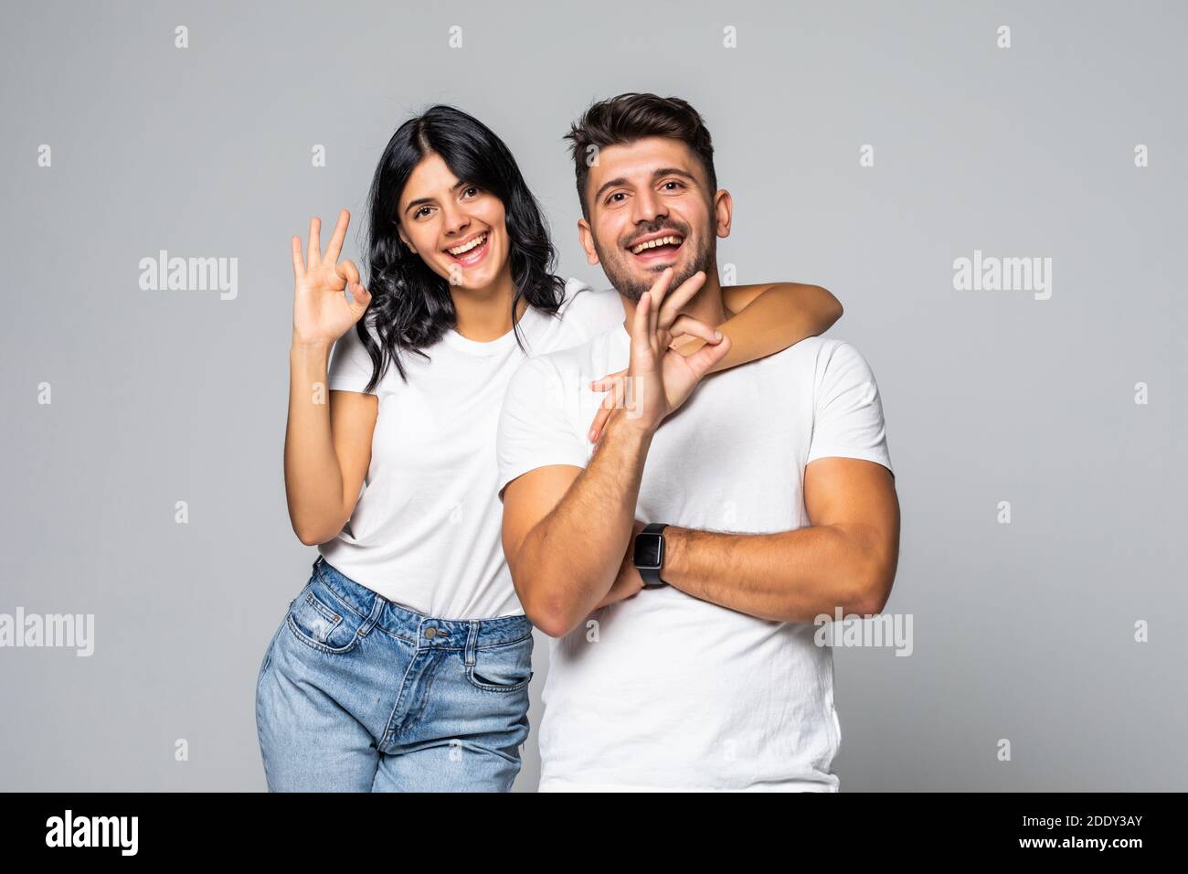 Full length portrait of a cheerful smiling couple hugging and showing ...